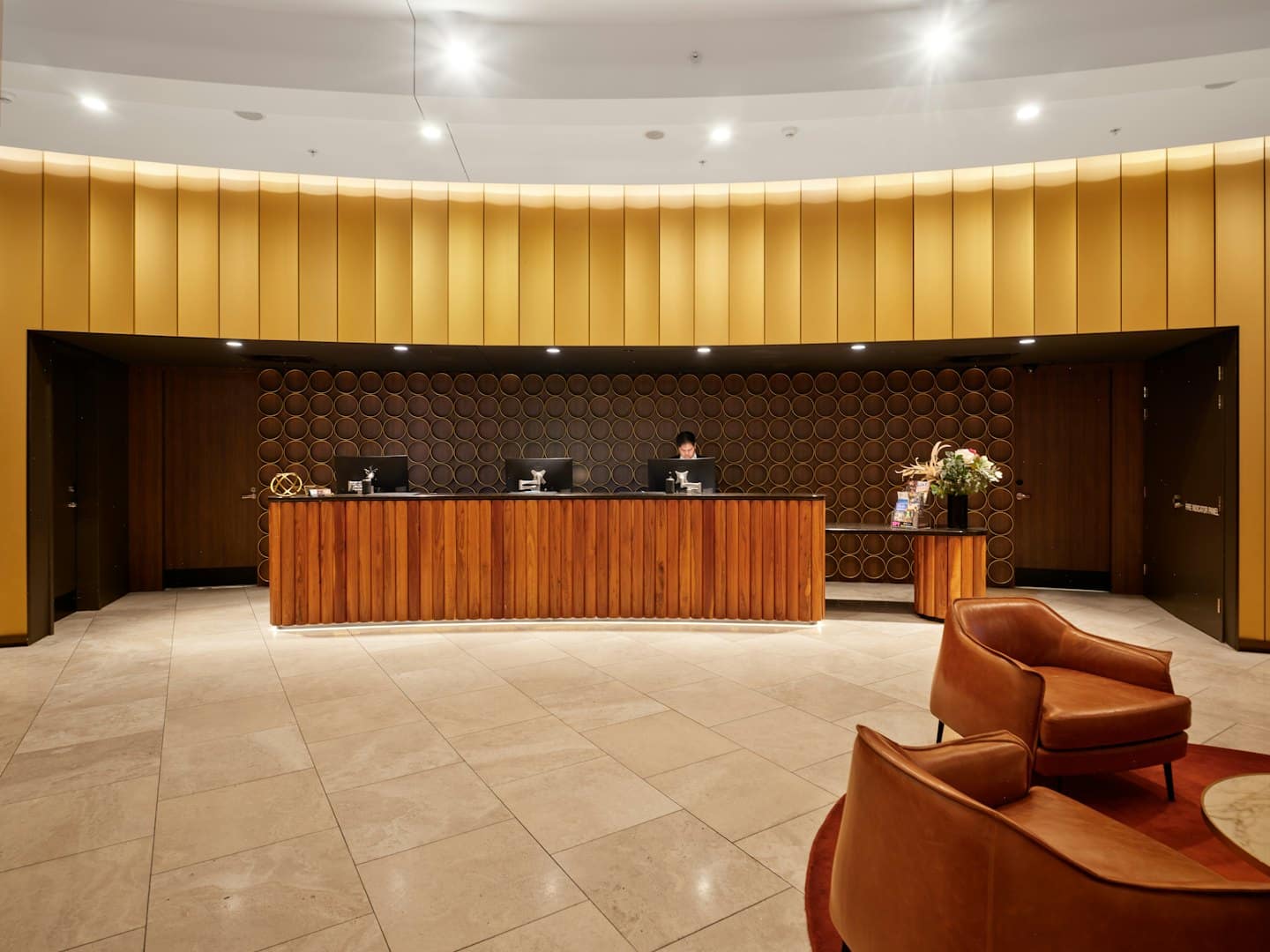 Hotel reception desk with person working and guest chairs.